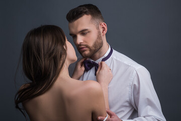 Passionate couple, romantic lovers. Woman holds mans bowtie, bow tie. Sexy elegant people in tender...