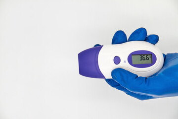 A hand in a protective glove holds an electronic non-contact thermometer. Temperature Measurement Device on white background © marketlan