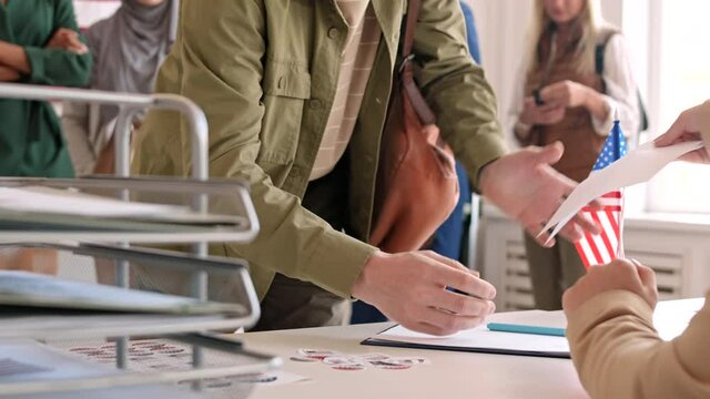 Close up of multiethnic people are coming to desk in the electoral district, signing document and taking their bulletin out of hands of young woman working there