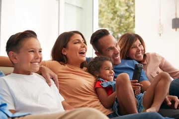 Fotobehang Multi-Generation Hispanic Family Relaxing At Home Sitting On Sofa Watching TV Together © Monkey Business