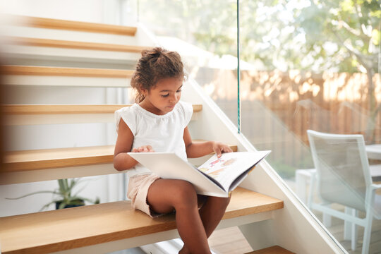 Hispanic Girl Sitting On Staircase In Modern Home Reading Book 