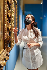 Woman visitor wearing an antivirus mask in the historical museum looking at pictures.