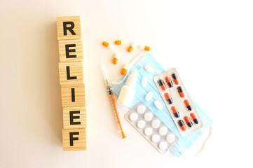 The word RELIEF is made of wooden cubes on a white background with medical drugs and medical mask. Medical concept.