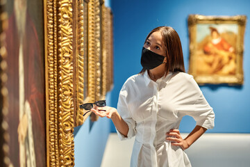 Woman visitor wearing an antivirus mask in the historical museum looking at pictures.