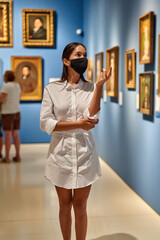 Woman visitor wearing an antivirus mask in the historical museum looking at pictures.