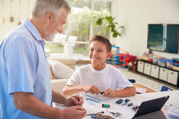Hispanic Grandson And Grandfather Building Robot From Electronic Components At Home Together