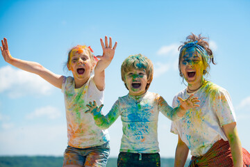 Funny kids face in color splash, coloured powder on children body. Cheerful friends showing hands painted in bright colors. Colorful dirty people.