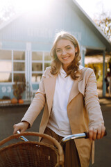 Happy young woman posing with bike on the background of a blue house. Autumn mood concept.