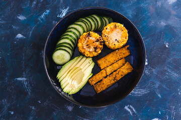 vegan nourish bowl with avocado cucumber polenta chips and spicy corn on the cob