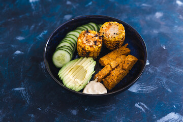 vegan nourish bowl with avocado cucumber polenta chips and spicy corn on the cob with vegan mayo