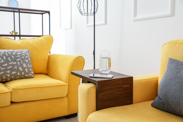 Glass of water and mobile phone on armrest table in room