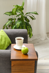 Cup of tea with apple on armrest table in room