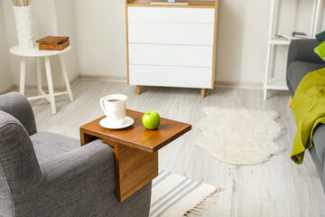 Cup of tea with apple on armrest table in room