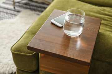 Glass of water with mobile phone on armrest table in room