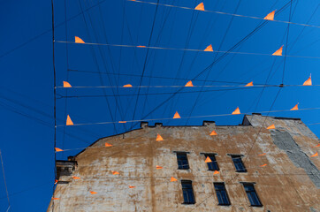 Waving flags on a grid of wires against the facade of a brown dilapidated house and a blue sky