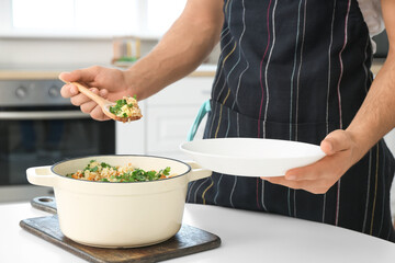Young man putting rice with vegetables on plate in kitchen, closeup