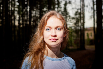 Portrait of cute blonde girl walking in forest outdoors. Nice woman posing on nature landscape with with pine trees.
