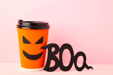Paper cup with Halloween face in the pink background with inscription boo