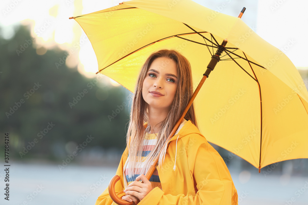 Wall mural Beautiful young woman with umbrella wearing raincoat outdoors