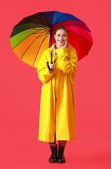 Beautiful young woman in raincoat and with umbrella on color background