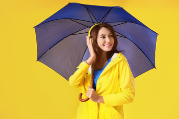 Beautiful young woman in raincoat and with umbrella on color background