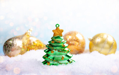 Fototapeta na wymiar Christmas festive background. Glass green christmas toy tree and blurred golden patterned christmas balls on white snow with bokeh. Close-up, copy space. Selective focus.