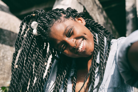 Happy young beautiful african american woman with pigtails and a piercing on her face makes selfie, beautiful smilling happiness and joy