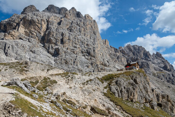 Mountain hut stands below an imposing mountain peak at the end of a steep trail. Catinaccio - Dolomites, Italy