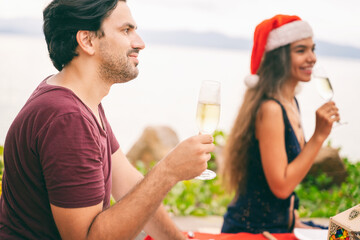 Attractive young man and woman celebrating christmas and new year on a tropical beach, holding glasses with champagne in their hands