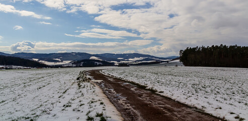 Hills and trees in winter Czech landscape with dirt road and snow field