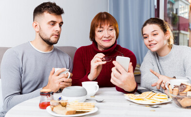 Happy senior woman with young couple absorbedly looking at phone at home