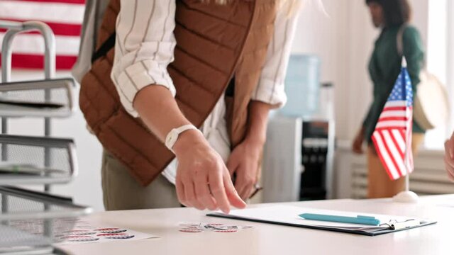Close up of diverse men and women are coming to desktop at the poll, signing document and taking sticker with the help of unrecognizable woman working there