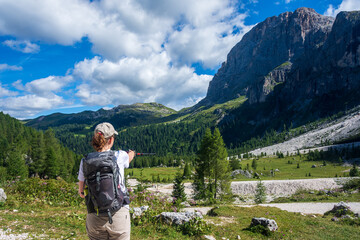 Fototapeta na wymiar Kid standing on a rock on the edge of the Alpine Bombasel Lake on Cermis Alps - Italy. Dolomite peaks are visible in the background and reflect in the water along with the clouds. Trentino, Italy