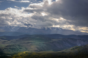 Dramatic dark clouds in mountains before storm. Landscape with mountain range, rain clouds and rays from the sun. Epic natural background.