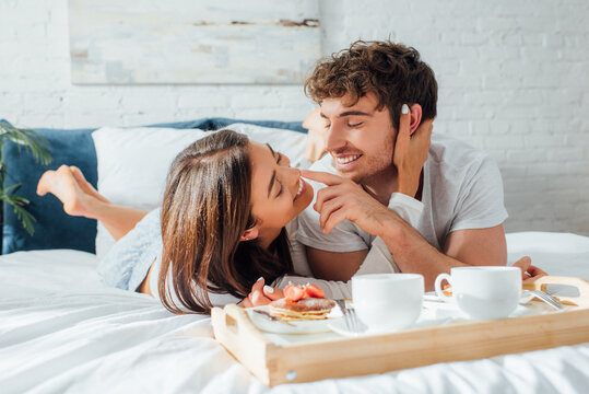 Selective focus of young couple touching each other near coffee and pancakes on breakfast tray on bed - Powered by Adobe
