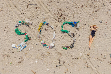 Fototapeta na wymiar SOS inscription and woman sunbathes on the beach nearby. Environmental problem. Ecology concept. Plastic on the beach with sos writing. Spilled garbage on the beach