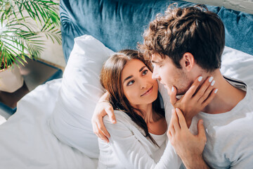 Selective focus of young woman touching boyfriend on bed at morning