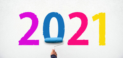hand holds paint roller and painting 2021 year on wall. happy new year 2021.
