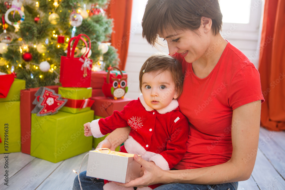 Wall mural young mother and her little daughter dressed as santa claus opening a magical christmas gift by a ch