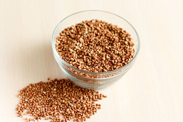 raw buckwheat in a glass cup, buckwheat seeds are scattered nearby