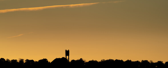 Water tank over the trees at dawn with orange sky