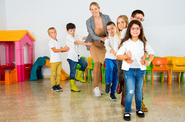 Happy smiling female teacher playing circle game with children in classrom