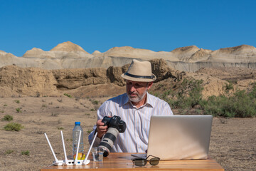 Photographer in hat working at table outdoors on laptop