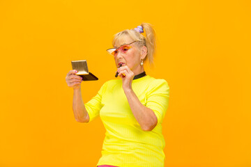 Fototapeta na wymiar Make up lover. Senior woman in ultra trendy attire isolated on bright orange background. Looks stylish and fashionable, forever young. Caucasian model in sunglasses, bright attire and sneakers. Flyer