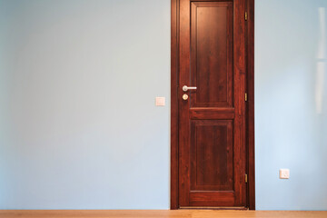 Frontal view to the wooden door in home interior room with wooden floors and blue walls.