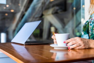 Portrait of a young woman sitting at the cafe and enjoying cup of coffee. The coffee bar is next to the train station of Lisbon, Portugal. Is a place with wooden tables and fresh tasty food.