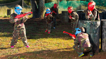 Teams of glad kids facing on battlefield in outdoor paintball arena