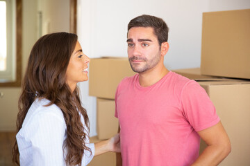 Young couple moving into new apartment, standing among carton boxes and discussing unpacking. Medium shot. New home concept