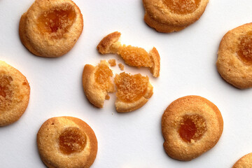 Seven handmade cookies with apricot jam arranged in even rows from an angle. One in the center is broken. on white background