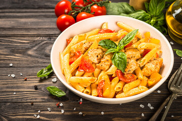 Pasta with chicken and vegetables at wooden table.